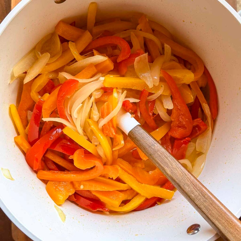 Bell peppers were added to the onions in a large pot. The bell peppers and onions have been sliced thin.
