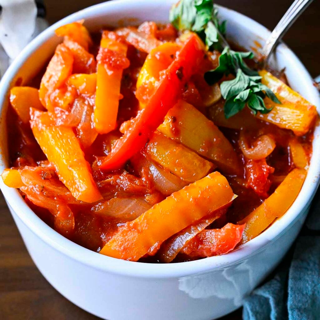 A white bowl filled with peperonata, stewed Italian bell peppers, pictured at a 15 degree angle