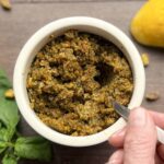 Pistachio pesto is a white jar with a hand holding the spoon filled with the pesto.