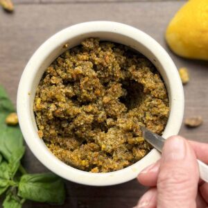 Pistachio pesto is a white jar with a hand holding the spoon filled with the pesto.