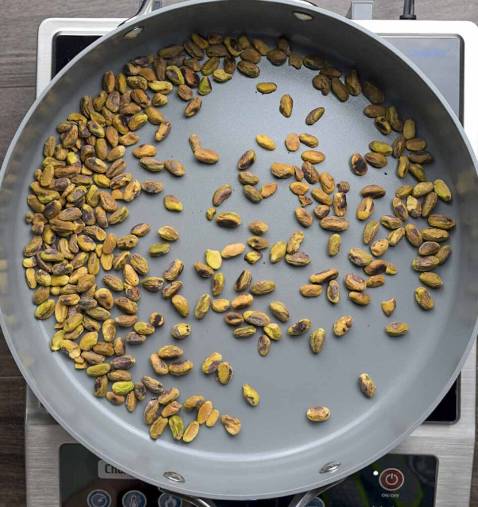 A large skillet filled with pistachios that are being toasted.