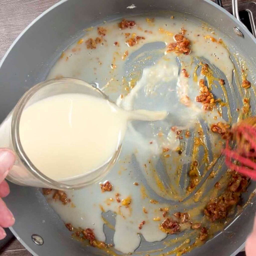 Adding milk to the butter, garlic, and sun-dried tomatoes to make creamy vegan pasta.