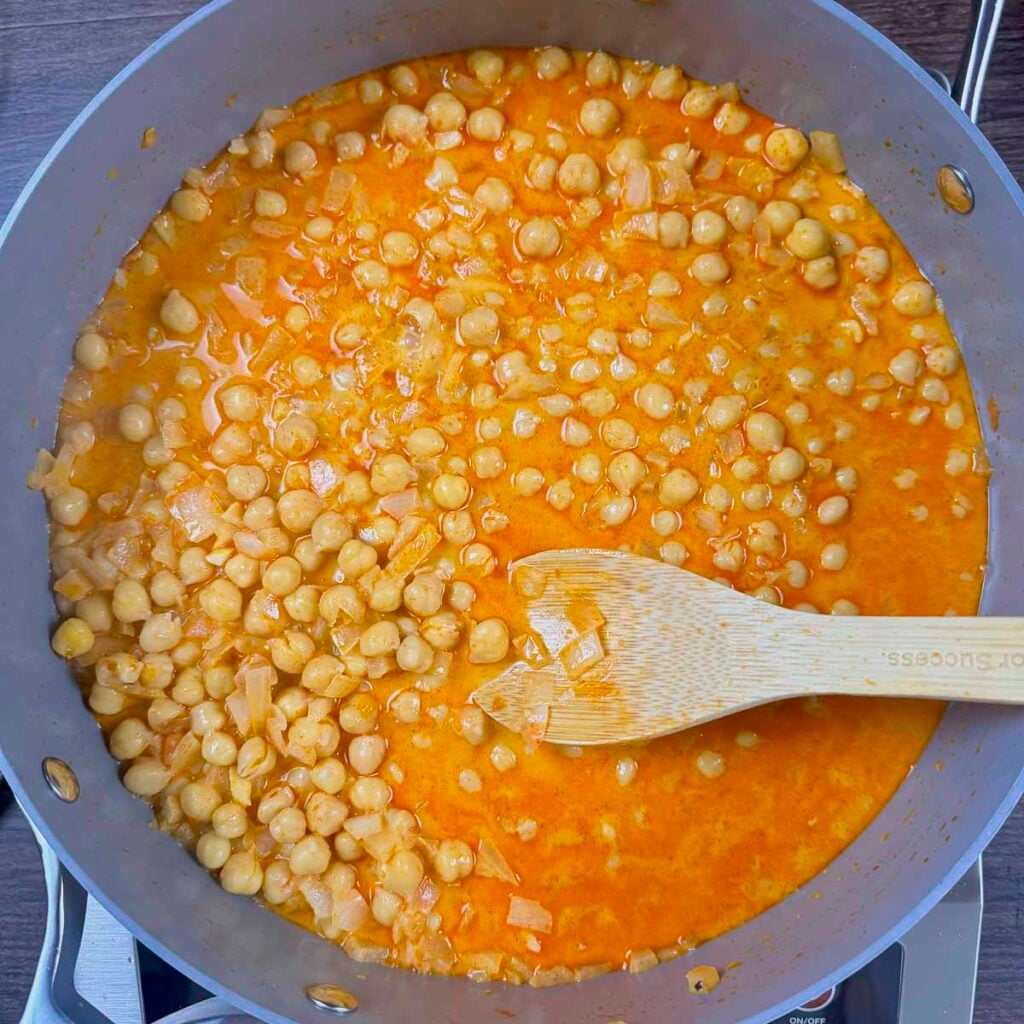 A large skillet filled with chickpeas simmering in a harissa coconut milk sauce.