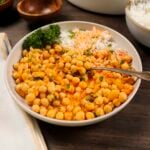 A plate filled with spicy Moroccan harissa chickpeas. The plate also has rice and is garnished with parsley and mint.