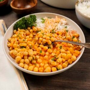 A plate filled with spicy Moroccan harissa chickpeas. The plate also has rice and is garnished with parsley and mint.