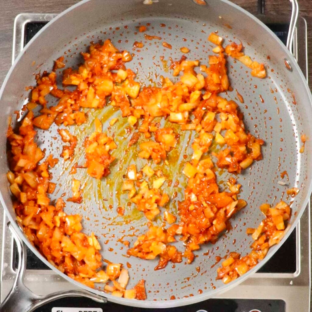 A skillet filled with harissa paste blooming with onions and garlic.