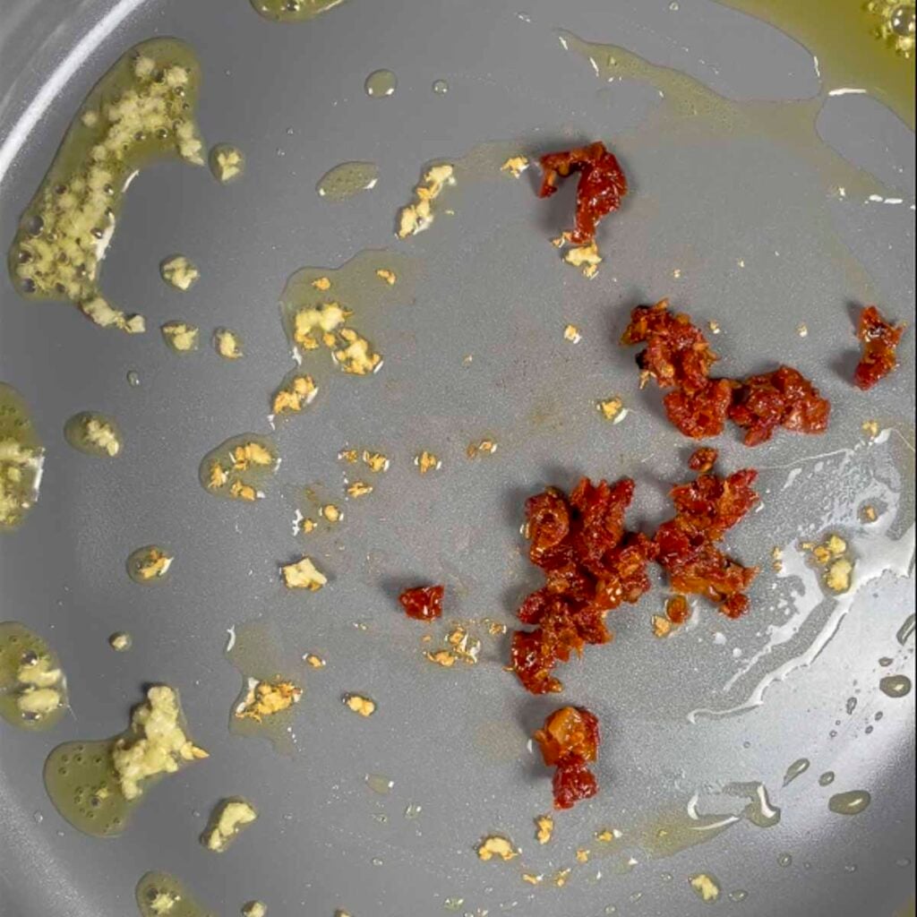 Sautéing garlic and sun-dried tomatoes for vegan alfredo sauce.