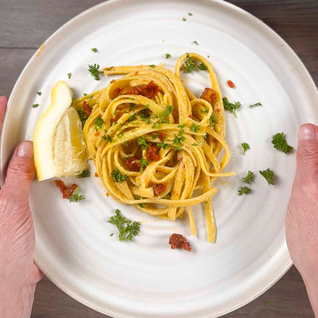 Hands holding a vegan pasta dish that has been garnished with parsley.