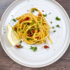 Vegan creamy pasta with sun-dried tomatoes on a white plate. The pasta has been garnished with parsley, sun-dried tomatoes, and parsley.