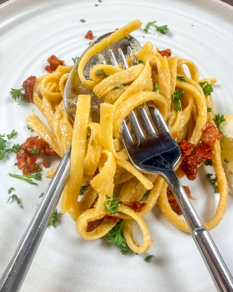 Creamy vegan pasta on a white plate that is twirled around a fork up close.