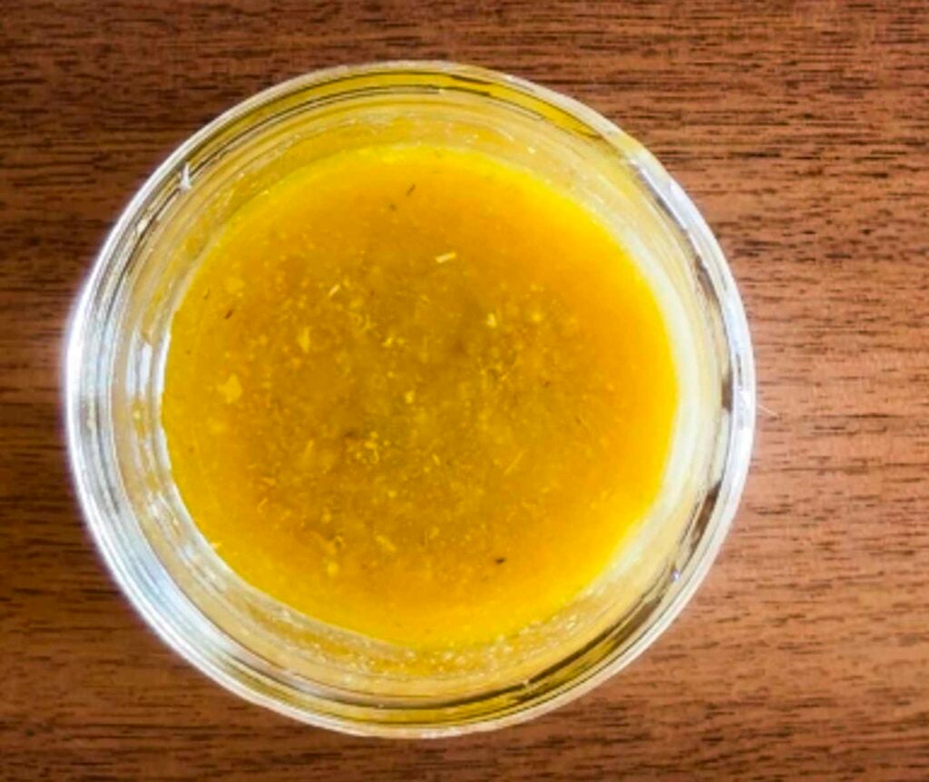 A small jelly jar filled with dressing used to make a Mediterranean couscous salad.