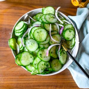 A bowl filled with a cucumber dill salad accented by a blue napkin.