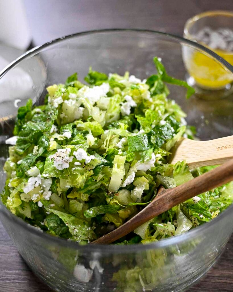 Greek lettuce salad salad in a large salad bowl garnished with feta cheese and lemon wedges.