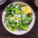 Maroulosalta salad in a wide white bowl garnished with feta cheese and lemon wedges.
