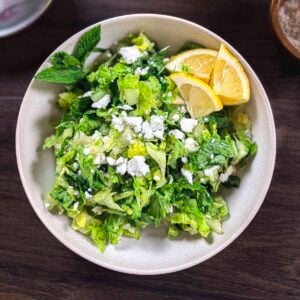 Maroulosalta salad in a wide white bowl garnished with feta cheese and lemon wedges.
