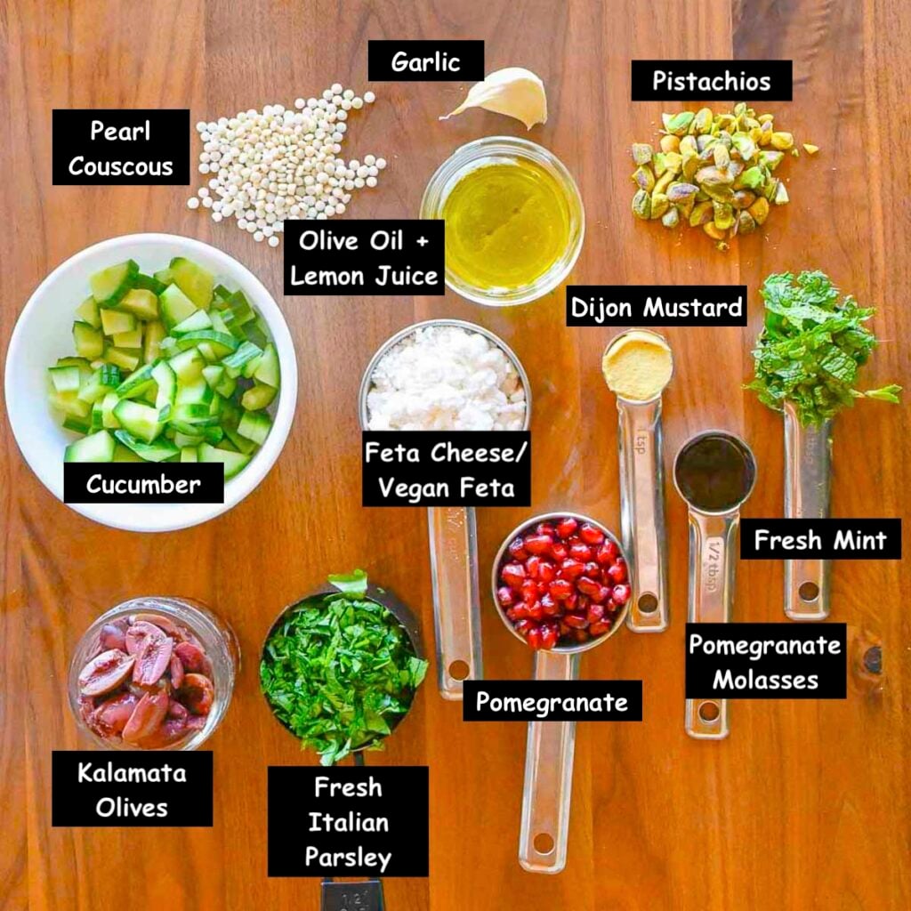 Ingredients used in making a Mediterranean couscous salad (pearl couscous, cucumbers, vegan feta cheese, kalamata olives, fresh italian parsley, pomegranate, pomegranate molasses, fresh mint, dijon mustard, pistachios, garlic, olive oil and lemon juice.)