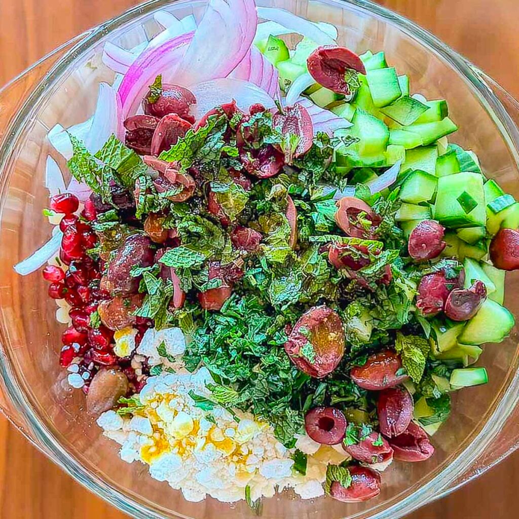 A bowl filled with Mediterranean couscous salad ingredients before being tossed together.
