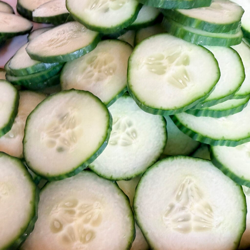A pile of thinly sliced cucumbers. All slices are evenly cut from using a mandoline set at 1/8.