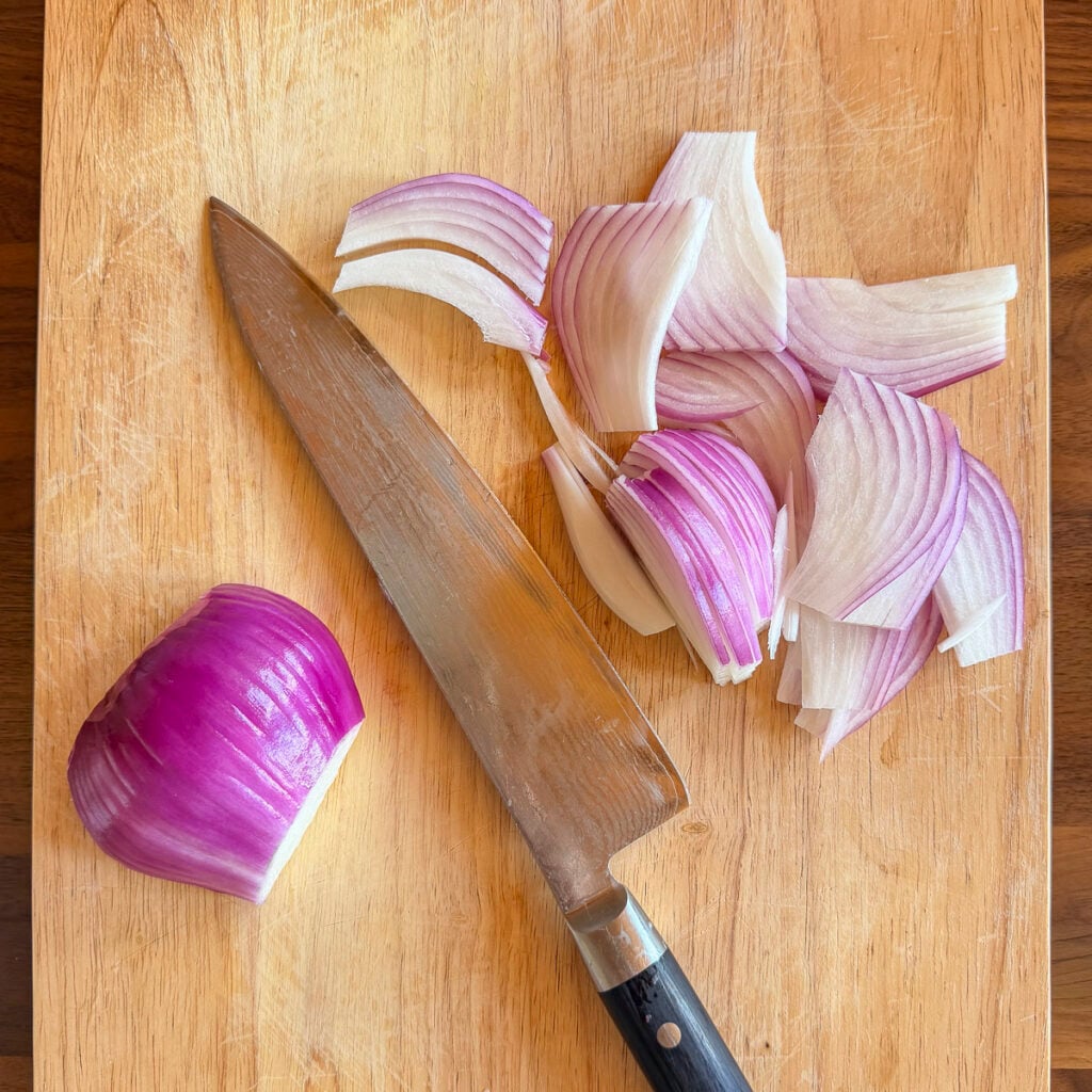 Red onions on a cutting board sliced thinly.