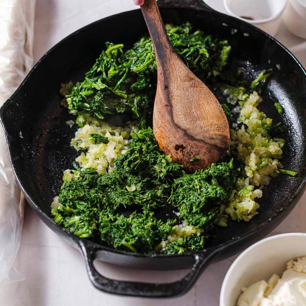A cast-iron skillet filled with frozen spinach, yellow onions, and green onions.