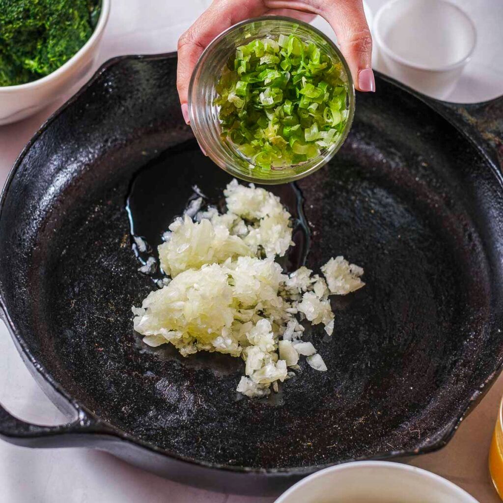 Adding onions to a cast-iron skillet.