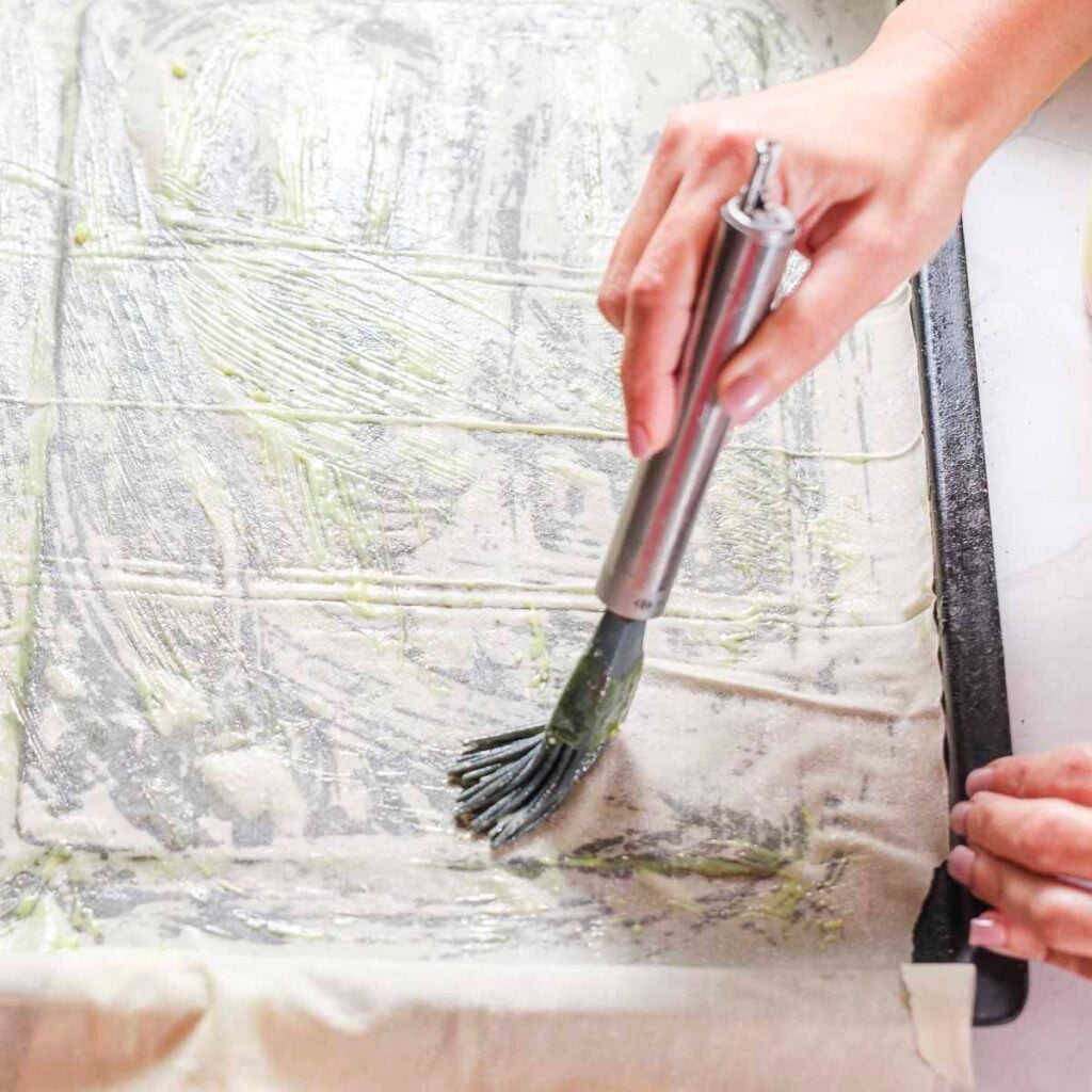 Brushing phyllo dough with plant-based butter while making vegan spanakopita.