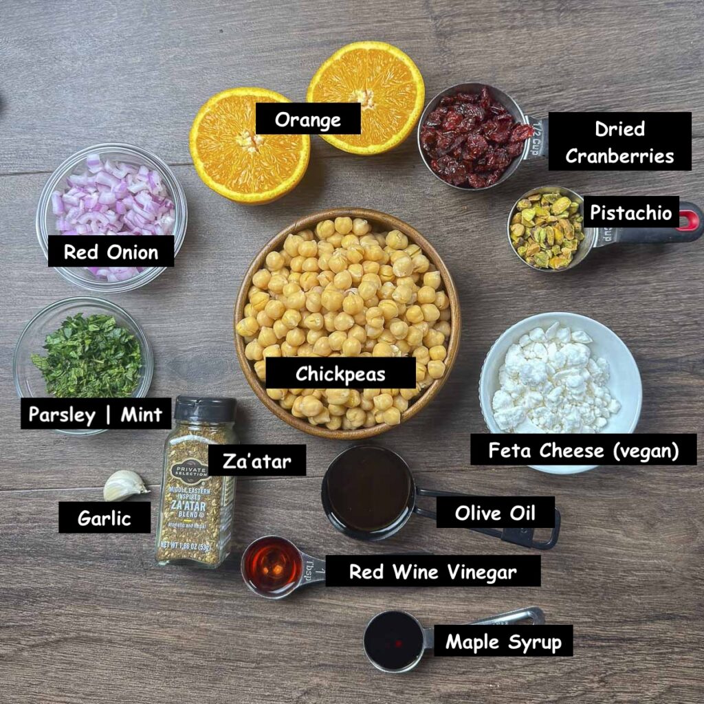 Ingredients used in making cranberry, chickpea and feta salad (chickpeas, feta cheese (vegan), dried cranberries, pistachios, orange, red onion, flat-leaf parsley, mint, garlic, za'atar, olive oil, red wine vinegar, and maple syrup.)