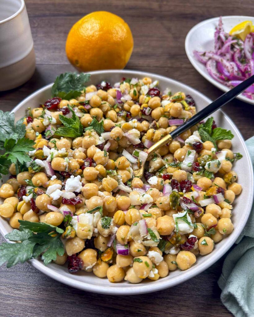 A plate filled with cranberry, chickpea, and feta salad that is garnished with mint and parsley.