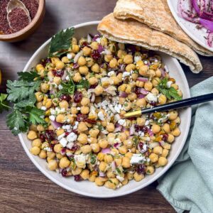 A plate filled with cranberry, chickpea, and feta salad that is garnished with pita pockets, mint, and parsley.