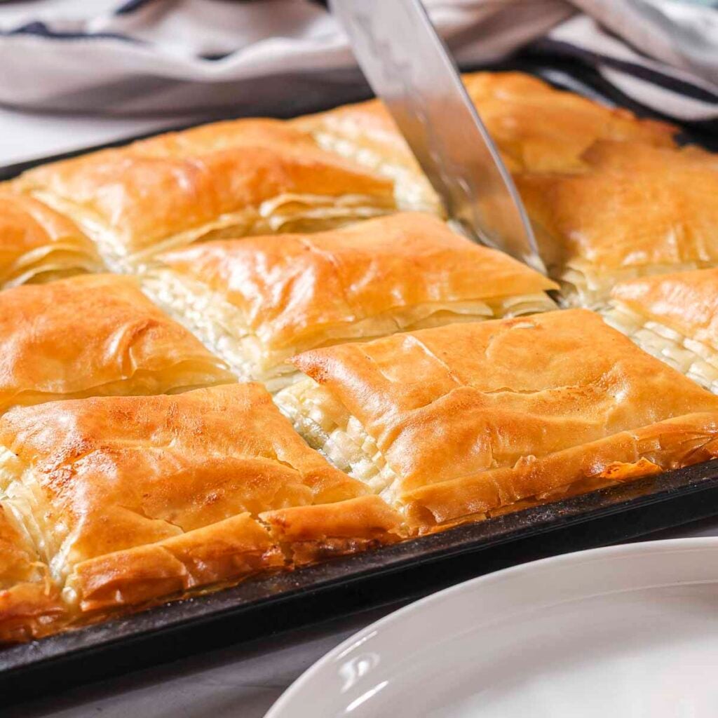 Cutting a square of baked plant-based spanakopita.