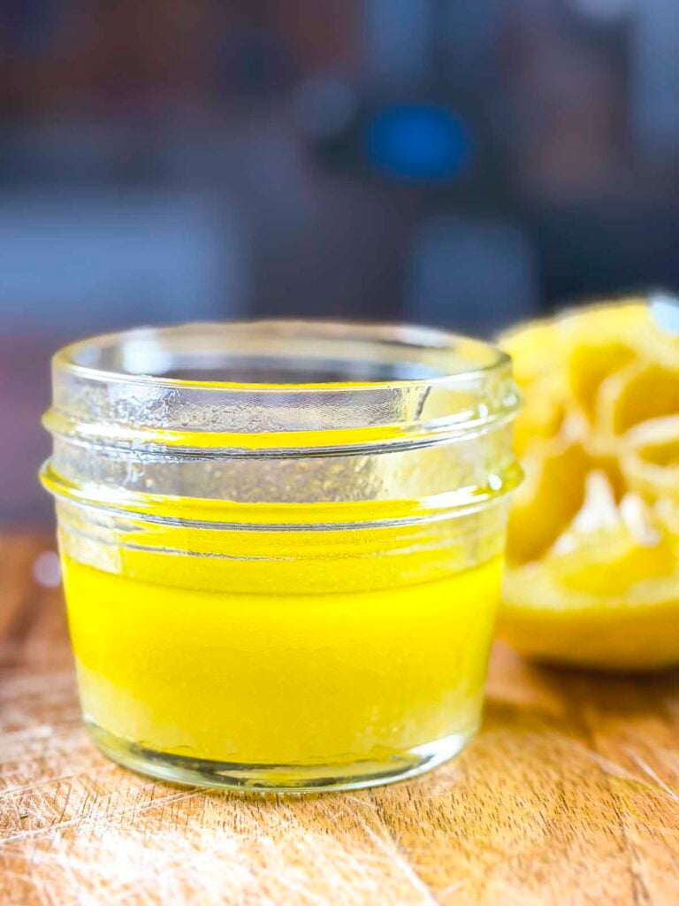 Ladolemono Greek olive oil lemon dressing mixed together in a small jelly jar with a squeezed lemon behind the jar.