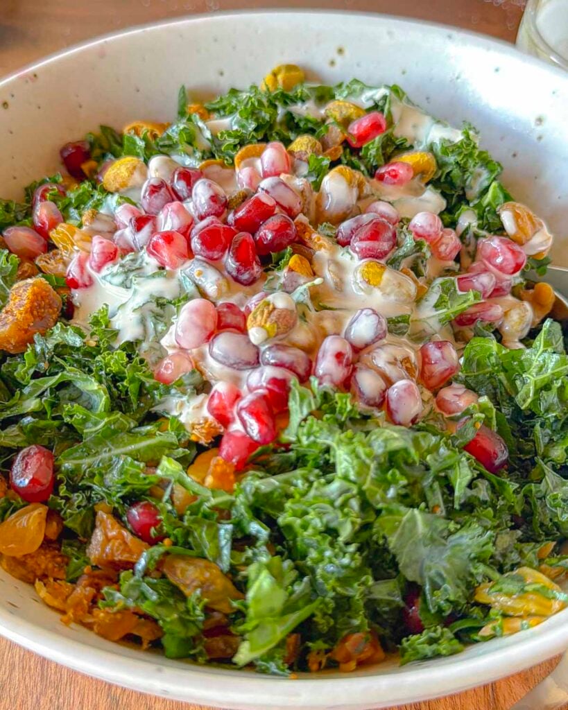 Kale salad topped with tahini dressing, pomegranate, golden raisins, pistachios, and figs.