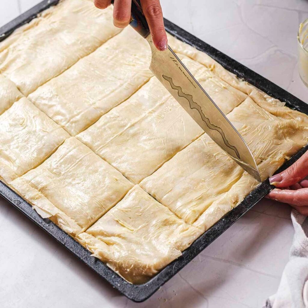 A knife is doing a precut on vegan spanakopita before being baked.
