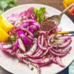 A spoon filled with sumac being sprinkled on top of red onions
