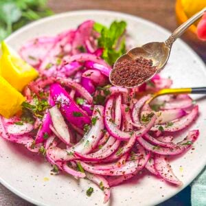 A spoon filled with sumac being sprinkled on top of red onions