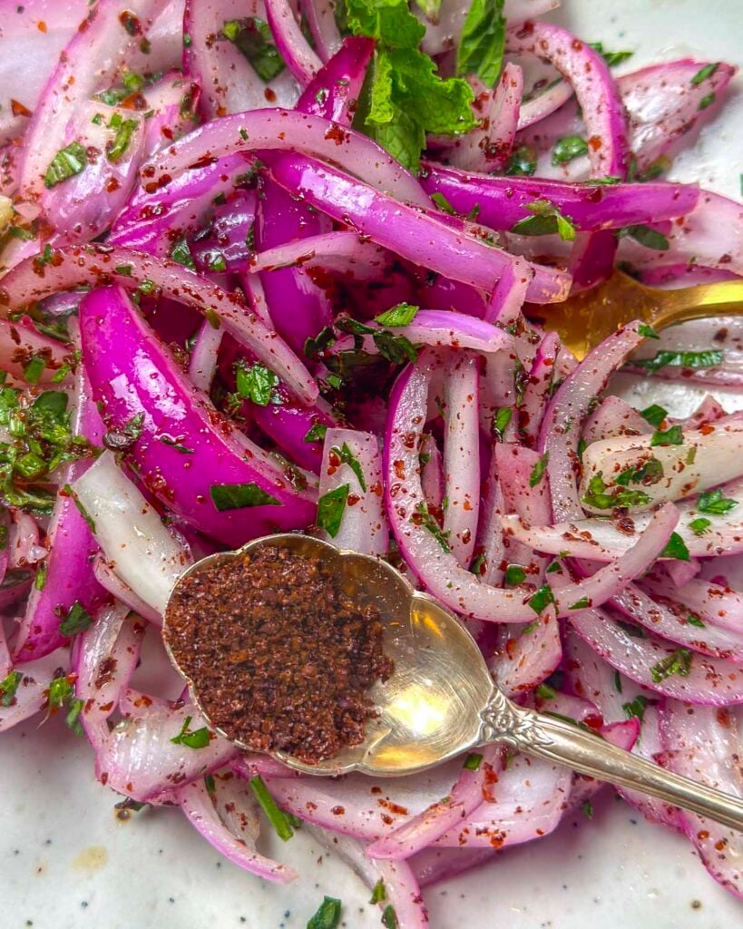 Turkish sumac onions on a plate with a spoon filled with extra sumac.