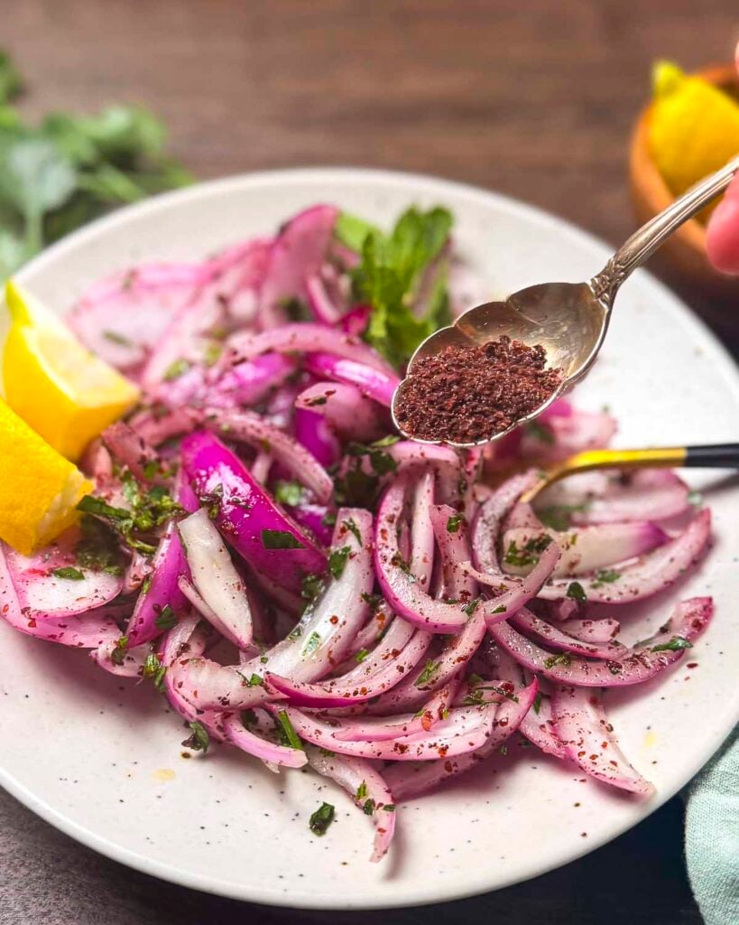 Turkish sumac onions on a plate with a spoon filled with extra sumac.