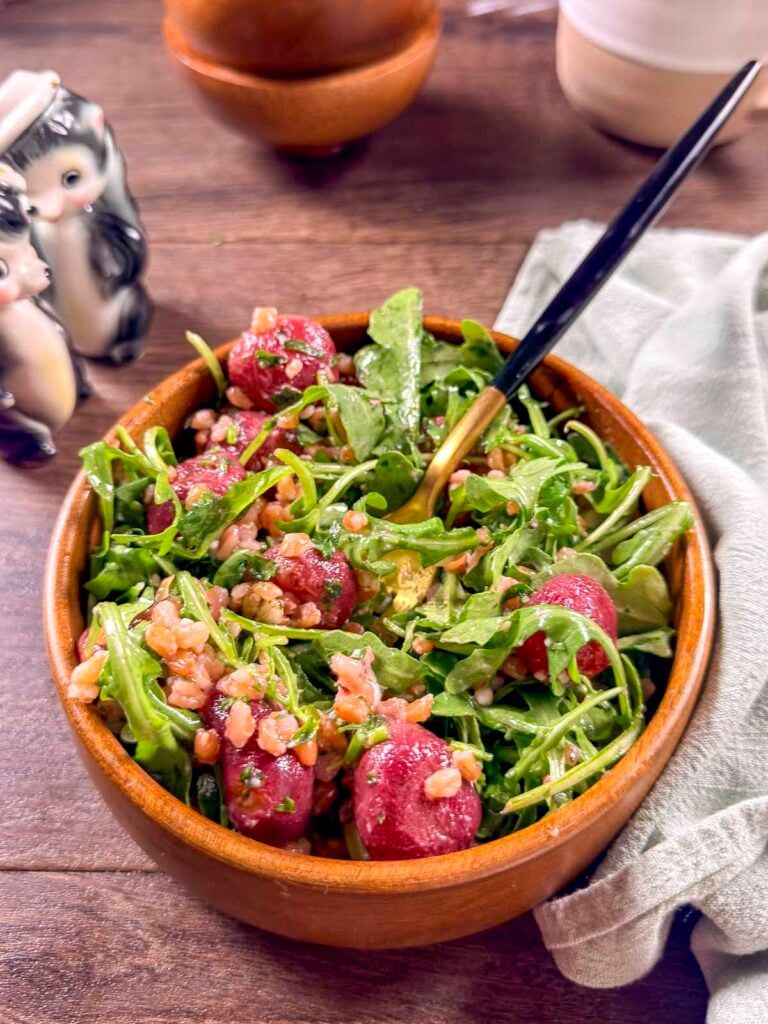 Grain salad with blistered roasted grapes, arugula, green onions, mint, and vegan feta in a small wooden bowl.