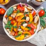 Grilled peach panzanella piled on a large white bowl with basil and mint.