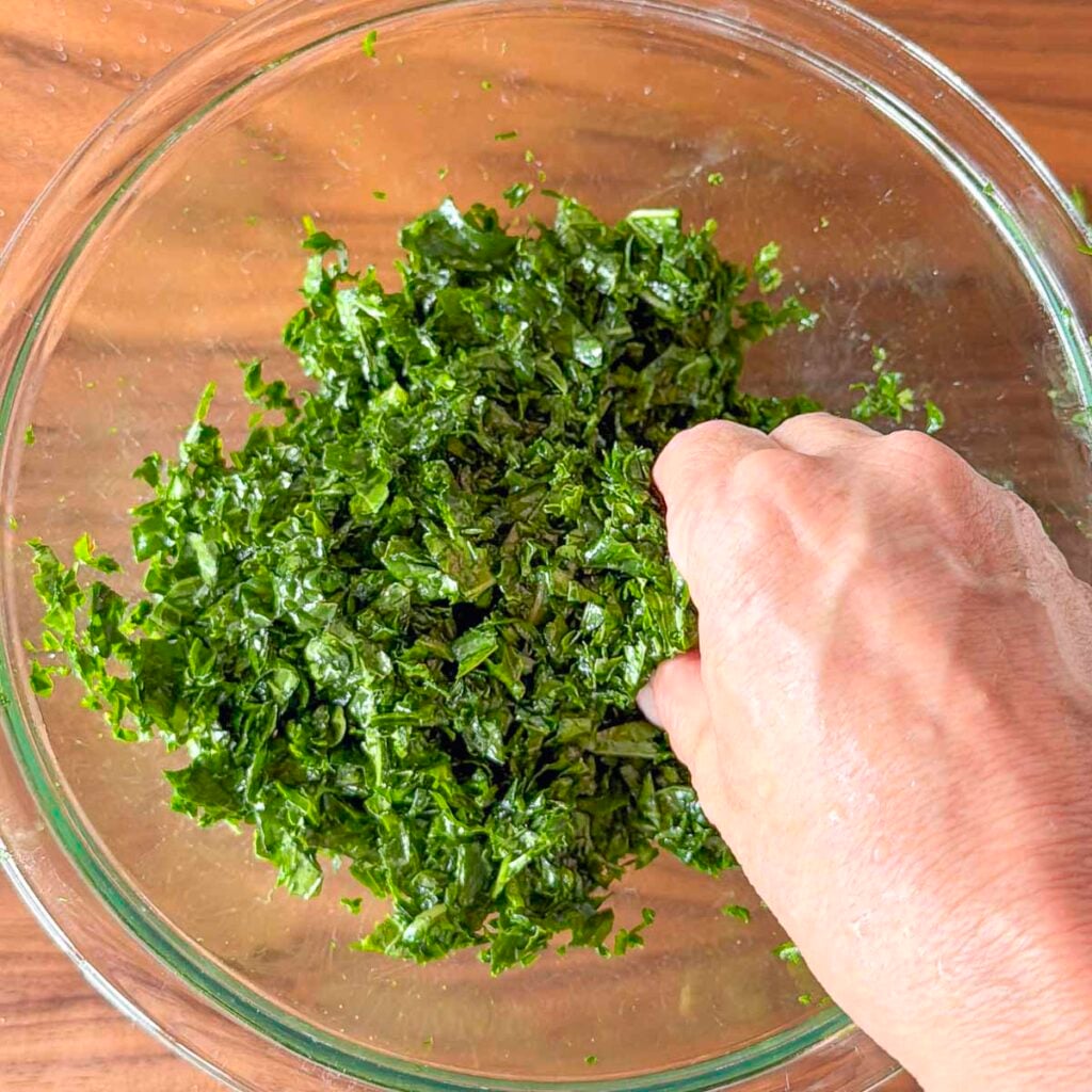 A hand massaging kale with olive oil and salt for a Mediterranean kale salad.