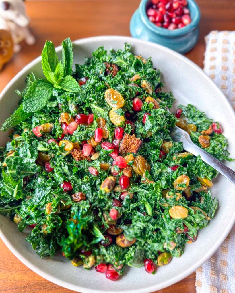 Mediterranean kale salad with tahini dressing topped with pomegranate arils, golden raisins, and dried figs.