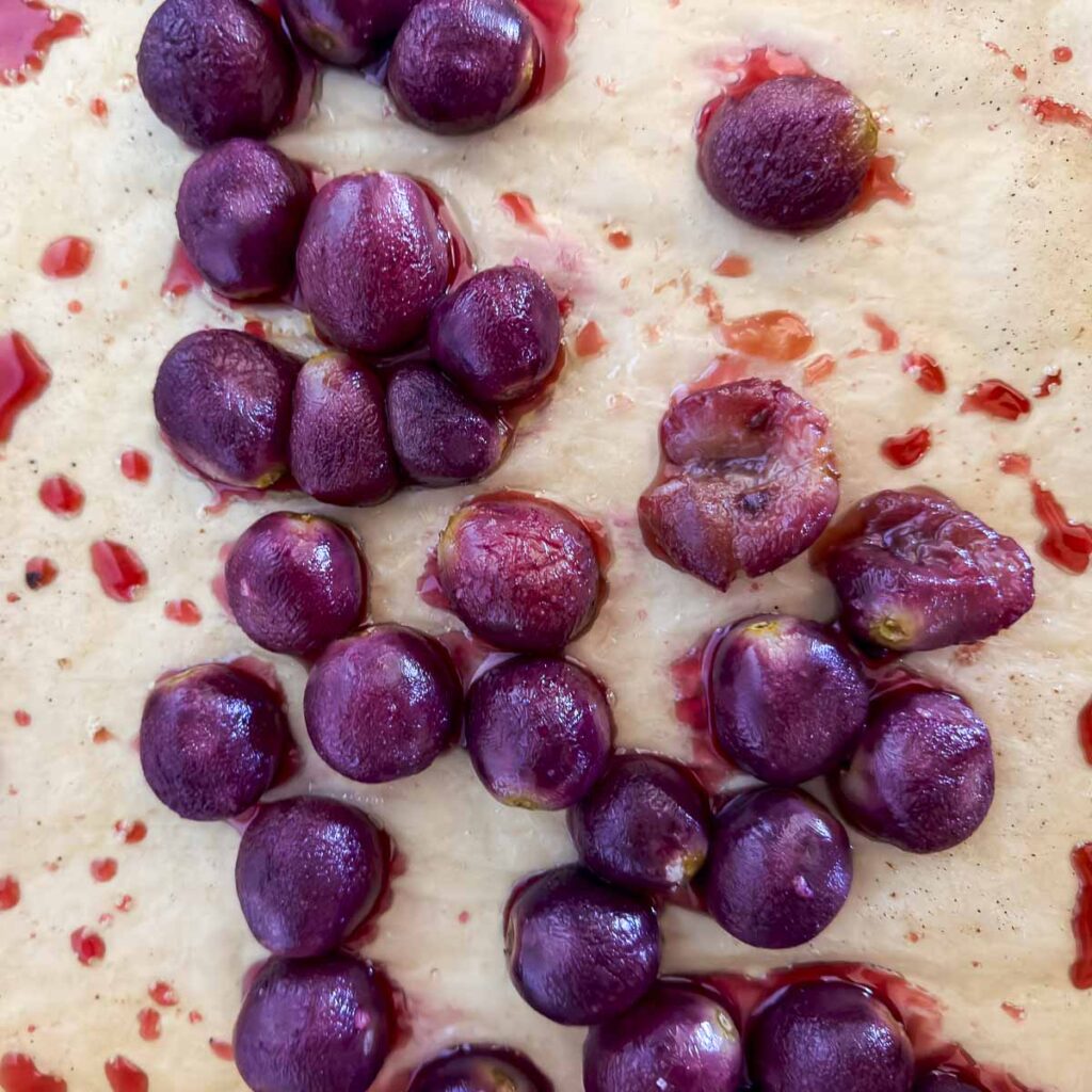A parchment-lined baking sheet filled with roasted red grapes.