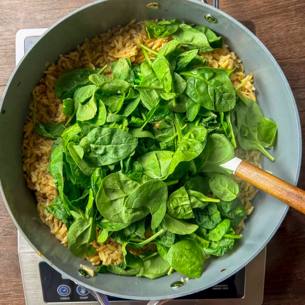 Adding fresh spinach to cooked orzo.