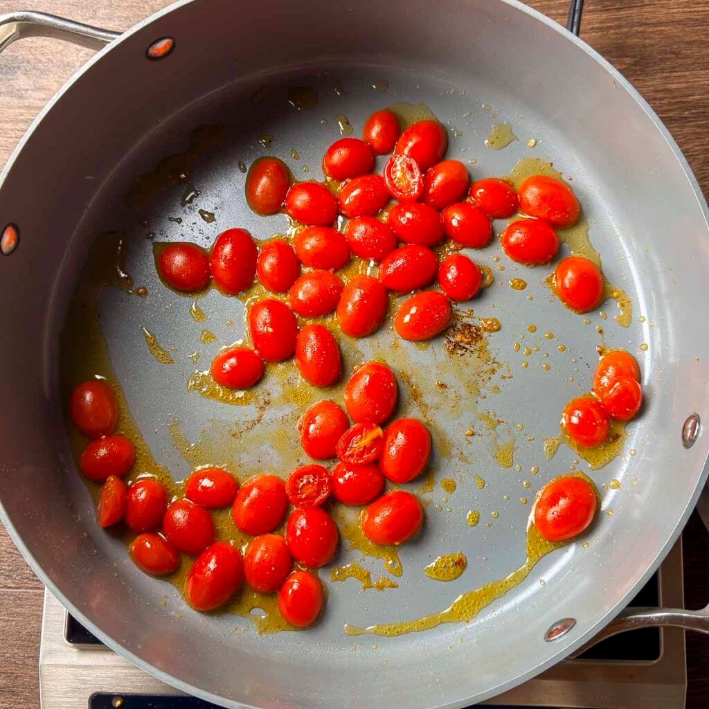 Blistering grape tomatoes that have been cut in half.