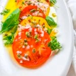 Marinated red and yellow heirloom tomatoes that have been garnished with diced shallots and capers.