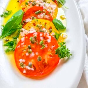 Marinated red and yellow heirloom tomatoes that have been garnished with diced shallots and capers.