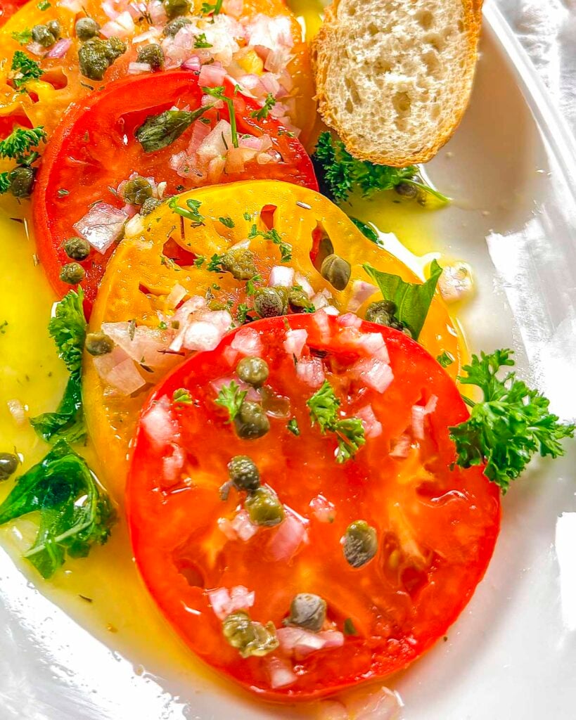 Marinated red and yellow heirloom tomatoes that have been garnished with diced shallots and capers.