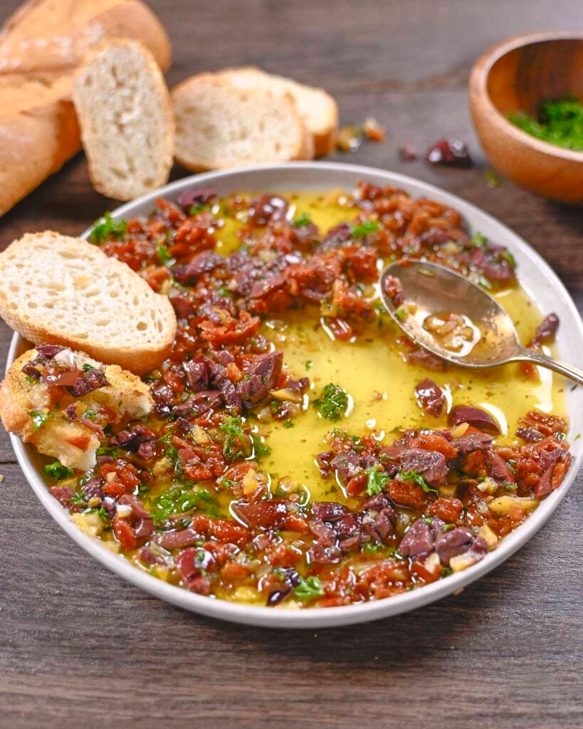 Sun-dried tomato dip made with Kalamata olives, sun-dried tomatoes, and olive oil with a spoon on the plate and a toast point.