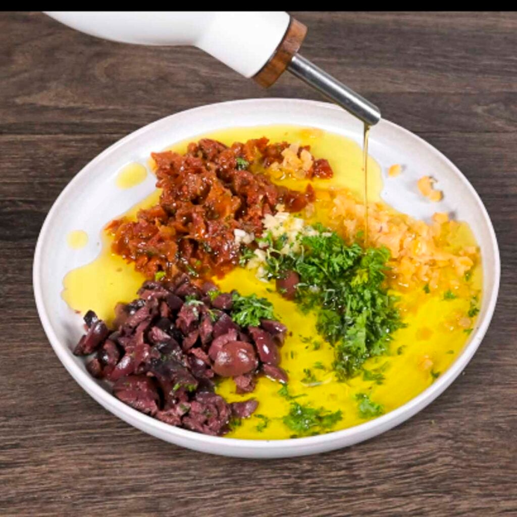 Mediterranean bread dip ingredients on a plate with the olive oil being added.