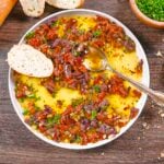 Mediterranean bread dip made with Kalamata olives, sun-dried tomatoes, and olive oil with a spoon on the plate and a toast point.
